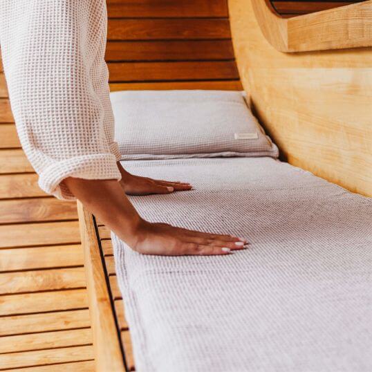 Eine Frau streicht ihre gepolsterte Saunaauflage glatt. Am Kopfende liegt ein Saunakopfkissen.