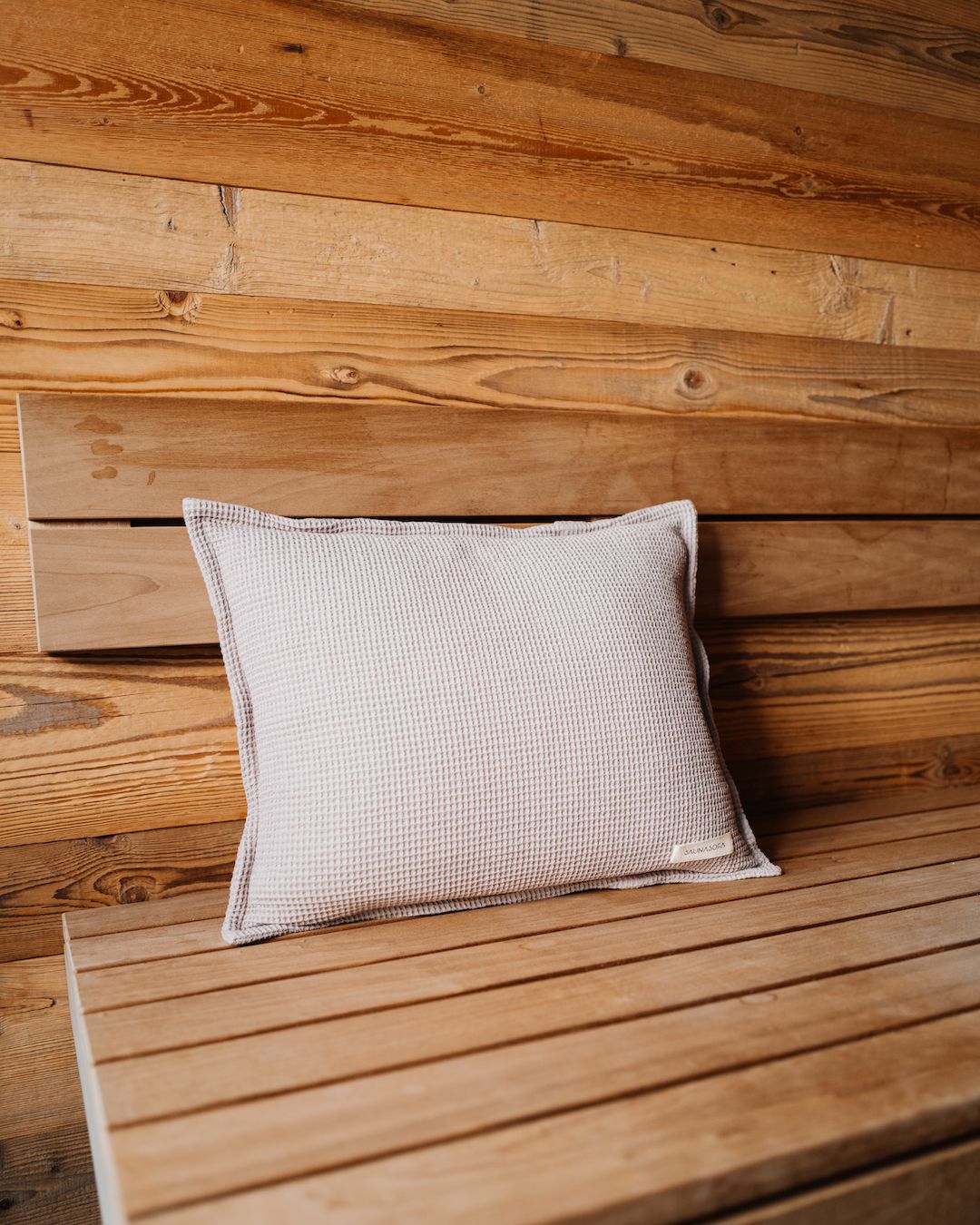 Ein Kopfkissen für die Sauna in der Farbe Taupe steht aufgerichtet auf einer Saunaliege.