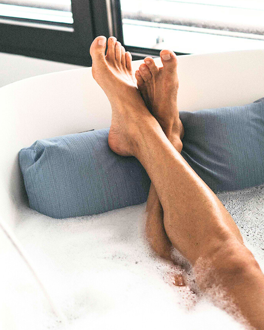 Die Füsse eines Mannes liegen entspannt auf einem Fusskissen in der Farbe Blau. 